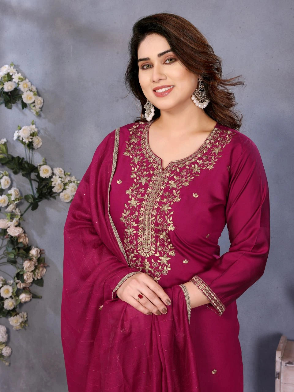 Woman wearing a magenta embroidered traditional outfit with a floral background
